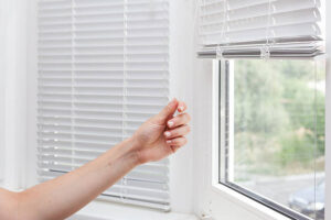 Woman adjusts the blind height on a window. Keeping blinds and curtains closed can keep your house cooler in the summer